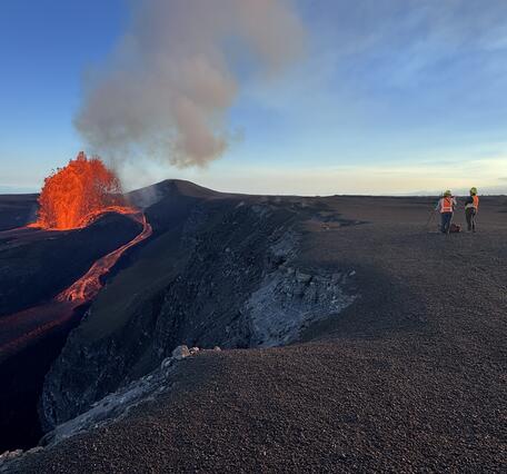 Color photograph of geologists on volcanic crater rim watching lava fountain