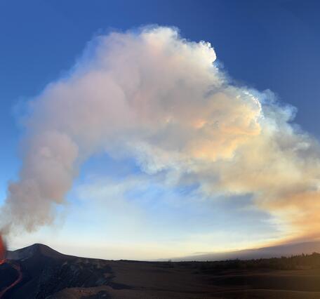 Color photograph of lava fountain and volcanic plume at sunset