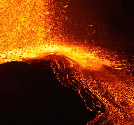 Color photograph of molten volcanic spatter landing in a lava flow