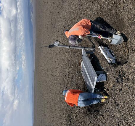 Color photograph of scientists fixing volcano monitoring equipment
