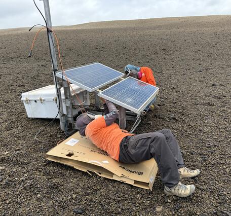 Color photograph of scientists fixing volcano monitoring station