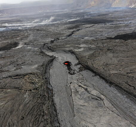 Color photograph of cooled lava channel that has tubed over with a spot of glow