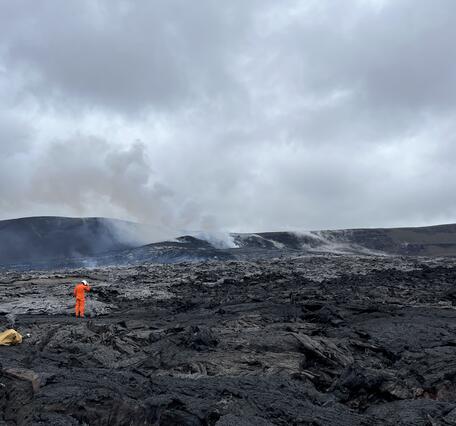 Color photograph of scientist on floor of crater with steaming volcanic vents in the background