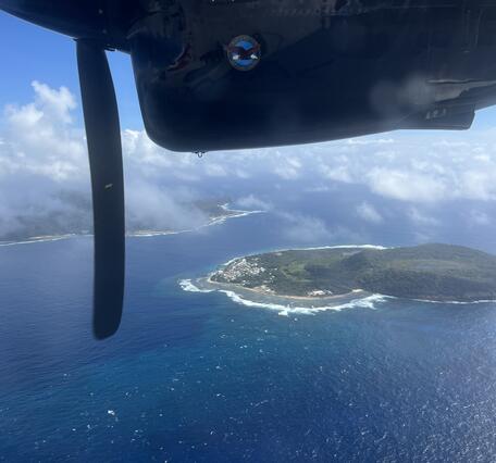 Color photograph of island with part of airplane visible in top of photo