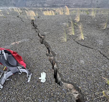 Color photograph of backpack next to cracks on ground