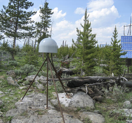 GPS antenna and solar panel in a lightly wooded area under partly cloudy skies