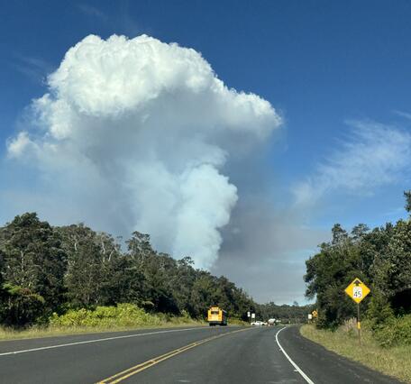 Color photograph of volcanic plume rising above road