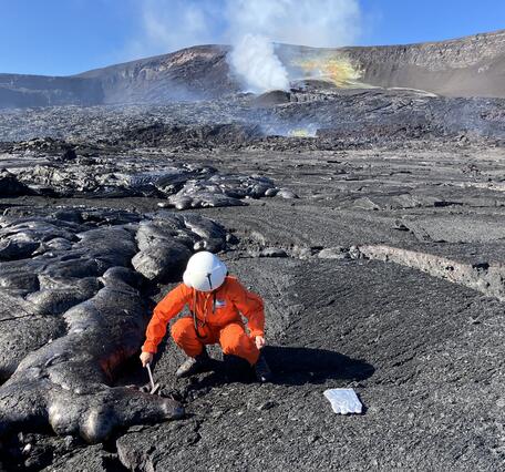 Color photograph of scientist collecting sample of cooled lava flow
