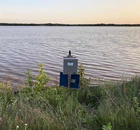 USGS streamgage on grassy lake shoreline at sunset
