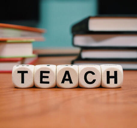 Lettered dice spelling out the word TEACH in the foreground with books in the background