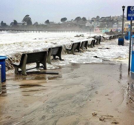 Parking spots and benches near a short seawall at the beach are inundated by winter waves. 