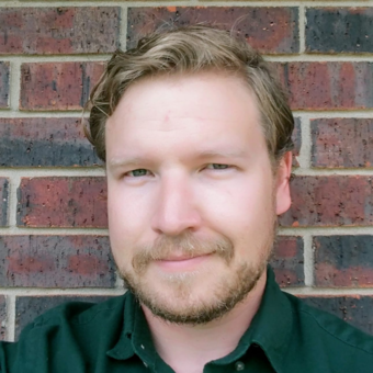 Headshot of Aaron Russell standing in front of a brick wall.