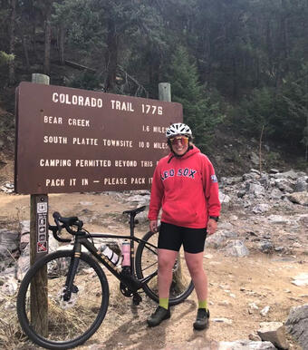 person in bicycle gear standing next to a bicycle in front of a location sign