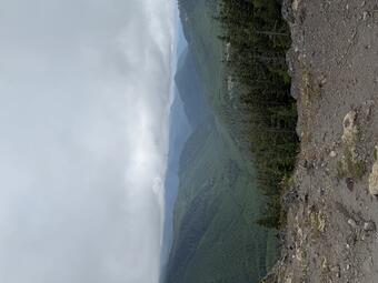 Barren ground in the foreground, with forested hills under cloudy sky in the background