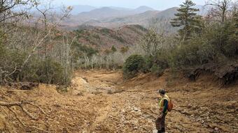person standing on mud and rocks looking downslope