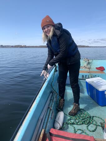Woman smiling standing on bow of boat holding on to rope to sample water