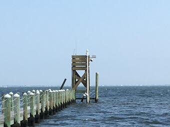 Looking out along a new pier at a tall four-pile structure hlding the new USGS Gage 