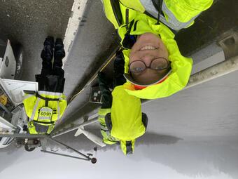 Bright yellow safety gear on USGS field crew stands out on a grey day as they work along a bridge over the river.
