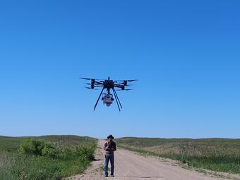 A person operates a drone in a grassland prairie