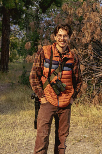 photo of matt hixson standing in a field with binoculars and a camera