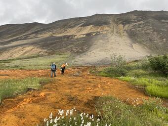 Two people walking across and orange seep.