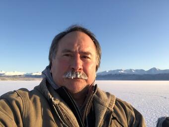 A man in a brown winter coat stands in a snowy landscape.