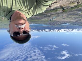 A man takes a selfie with snow-caped mountains in the distance