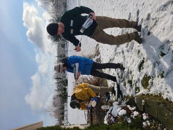 Three scientists collecting residential water well samples on sunny snowy day