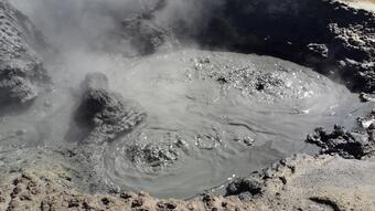 Boiling dark gray mud splashing within a small depression