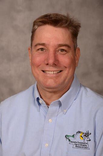 scientist smiling, with short blond/red hair, wearing a blue shirt