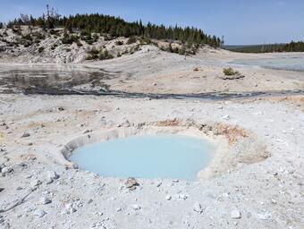 barren chalky ground with a milky-blue pool in the middle and a small hill with scrub vegetation in the background