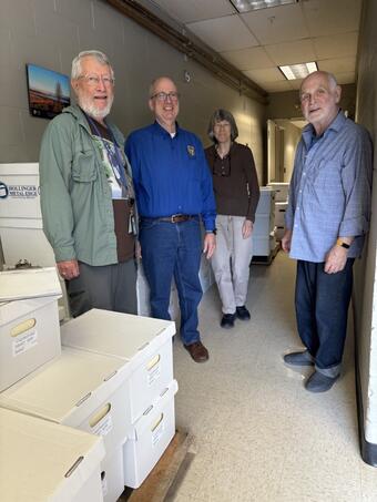 Three men and one woman stand in front of stacks of boxes containing Chans Robbins records. 