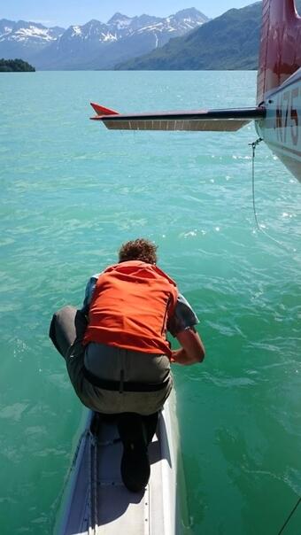 A scientist collects a water sample from a glacial lake next to a seaplane in Alaska