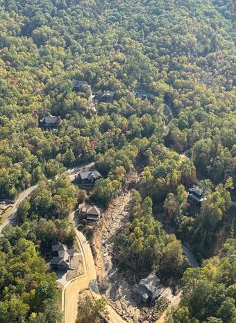 aerial view of forested area with landslide path visible near houses and road
