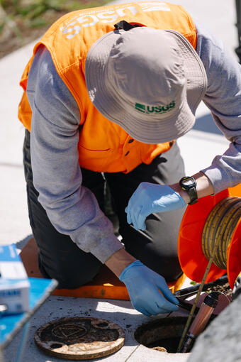 scientist looks at watch while lowering tape into well