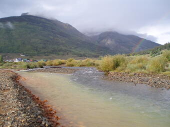 Orange and brown colored water in Cement Creek with mountains and a rainbow in the background