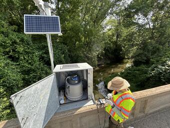 Scientist collecting field parameters and checking the autosampler at streamgage on bridge