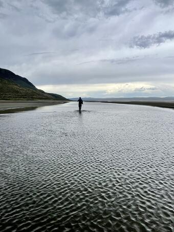 person in shilouette walking away from the camera in the shallows along a shoreline