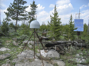GPS antenna and solar panel in a lightly wooded area under partly cloudy skies