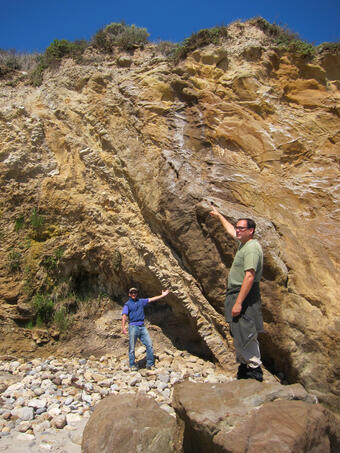 Two geologists pointing out faulted rocks