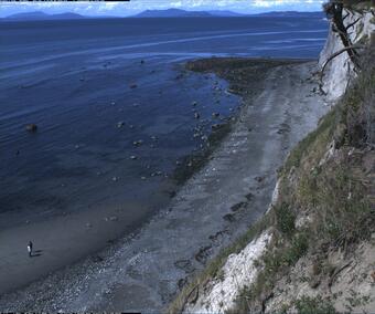 View from up high above a flat beach area lots of rocks and boulders, very little wave action.