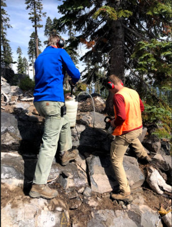 Two geologists stand on a rocky slope and use a modified chainsaw engine to drill rock cores