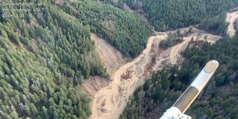 aerial view of muddy braided river surrounded by tree-covered hillslopes