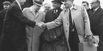 Black and white photo of two men shaking hands with other men standing in the background