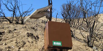 Solar panels, wires, and other equipment on a hillside devoid of vegetation.  