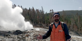 Man standing in front of a geyser with orange vest on