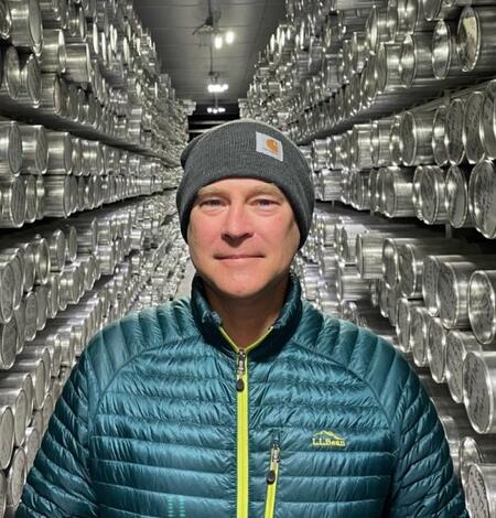 Image of man in blue jacket and gray hat standing between two rows of silver-wrapped ice cores. 