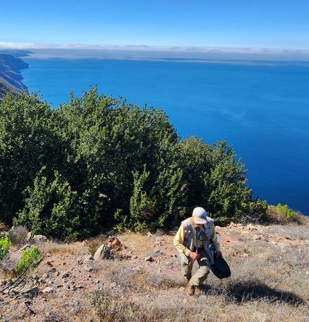Zoologist Charles Drost walks up a steep hill high above the coast on San Clemente Island, CA