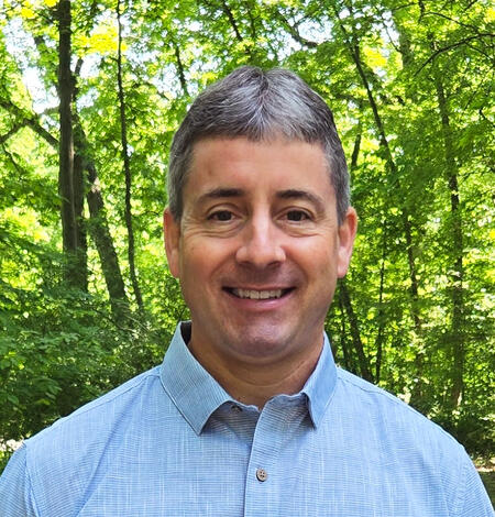 A researcher smiling standing in front of woods