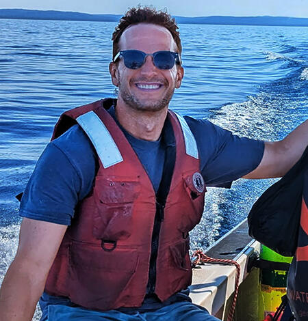 Researcher wearing a life vest sitting on a boat gunwale.